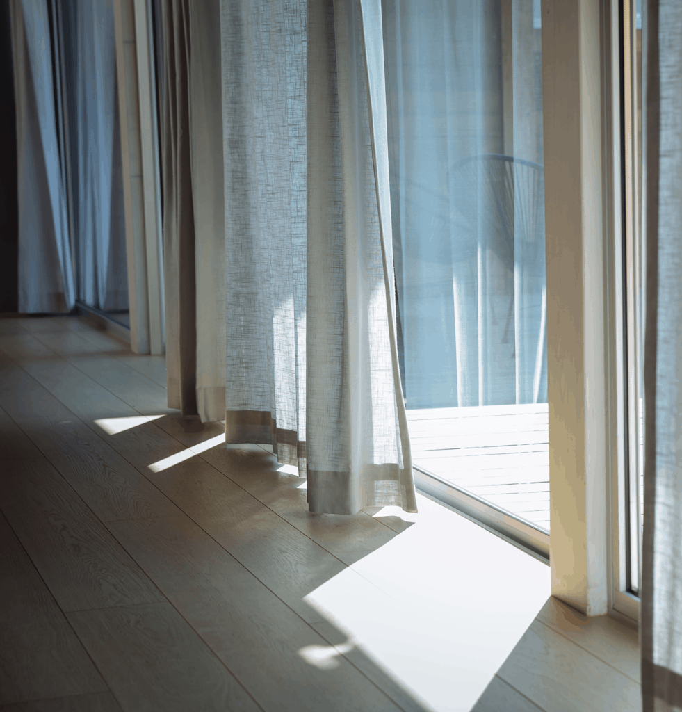 side on wide show of a beige curtain in front of a bright window